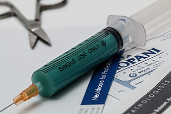 Medical syringe with green liquid on prescription form and surgical scissors