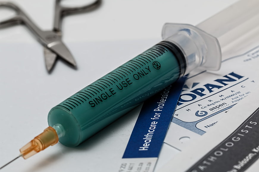 Medical syringe with green liquid on prescription form and surgical scissors