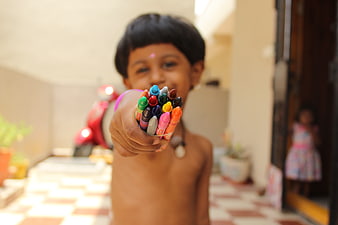Child holding colorful crayons towards camera
