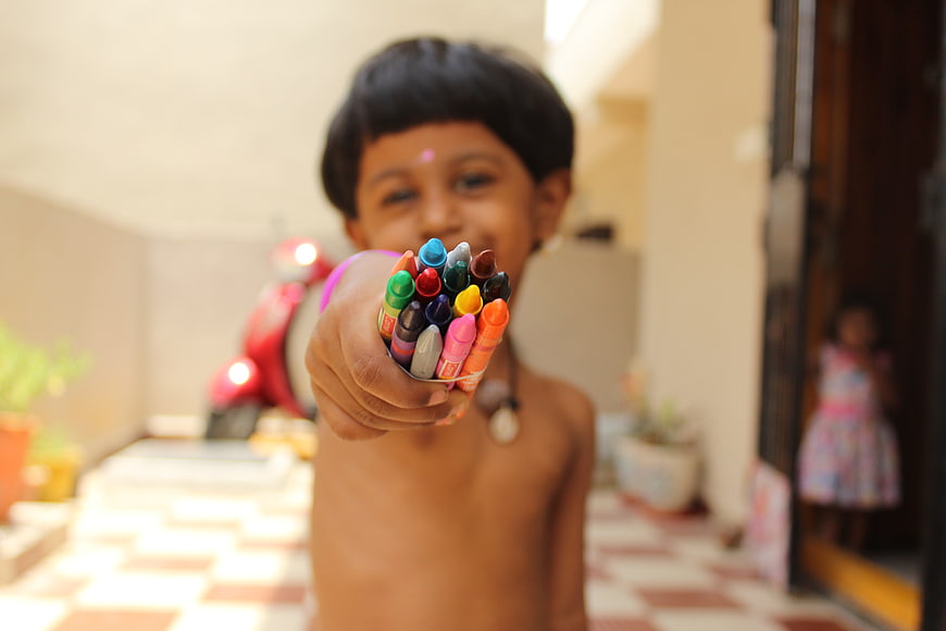 Child holding colorful crayons towards camera