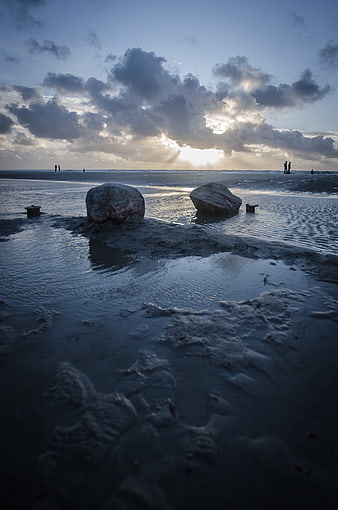Dramatic sunset over wet beach with large stones and silhouettes