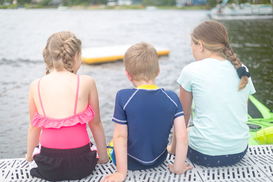 Three children sitting on a dock looking at the lake
