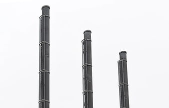 Three black industrial chimneys against white sky