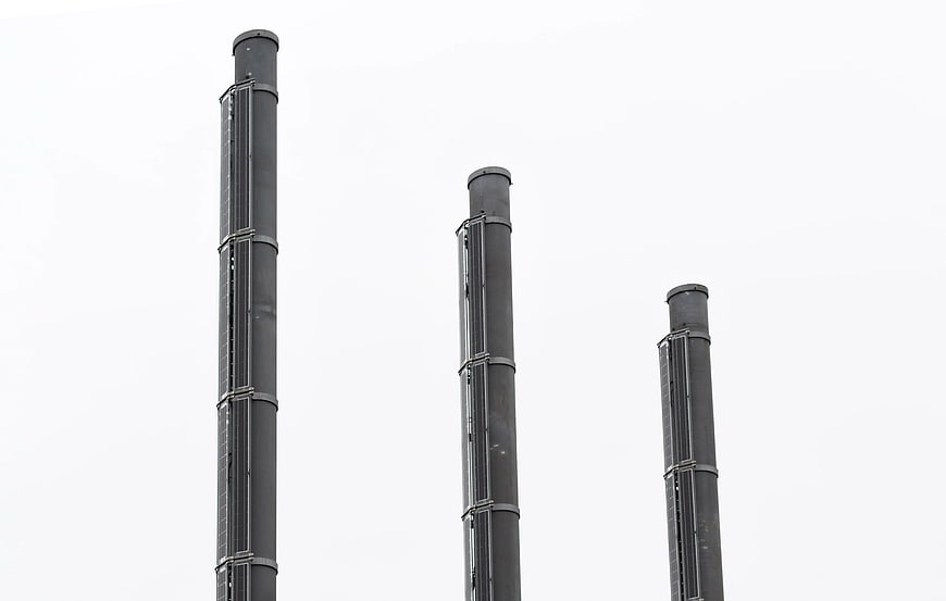 Three black industrial chimneys against white sky