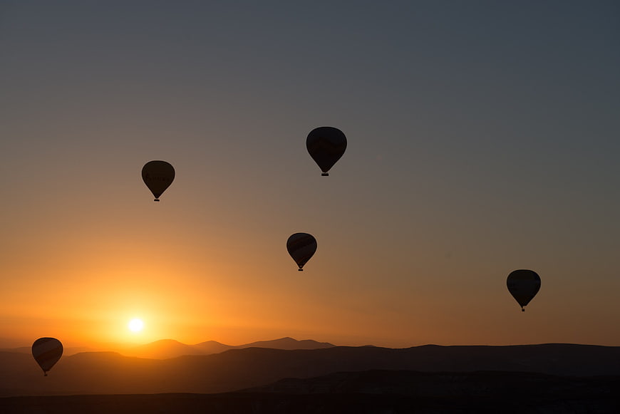 Silhouetted Hot Air Balloons Flying Over Mountains at Sunrise