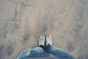 First-person view of white shoes standing on sandy beach