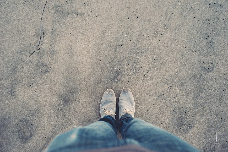 First-person view of white shoes standing on sandy beach