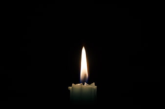 Single lit candle flame glowing against a pitch black background