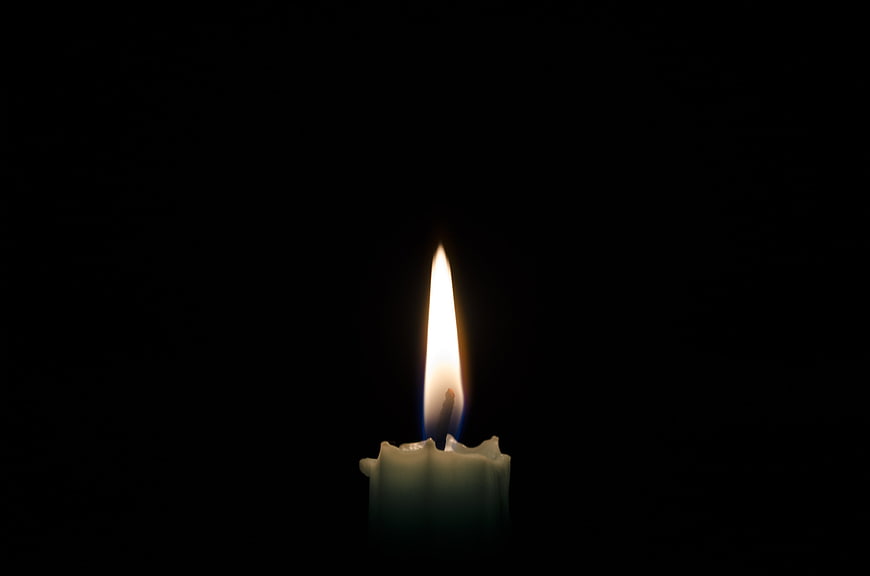 Single lit candle flame glowing against a pitch black background