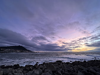 Dramatic purple sunset over rocky coastline with ocean waves