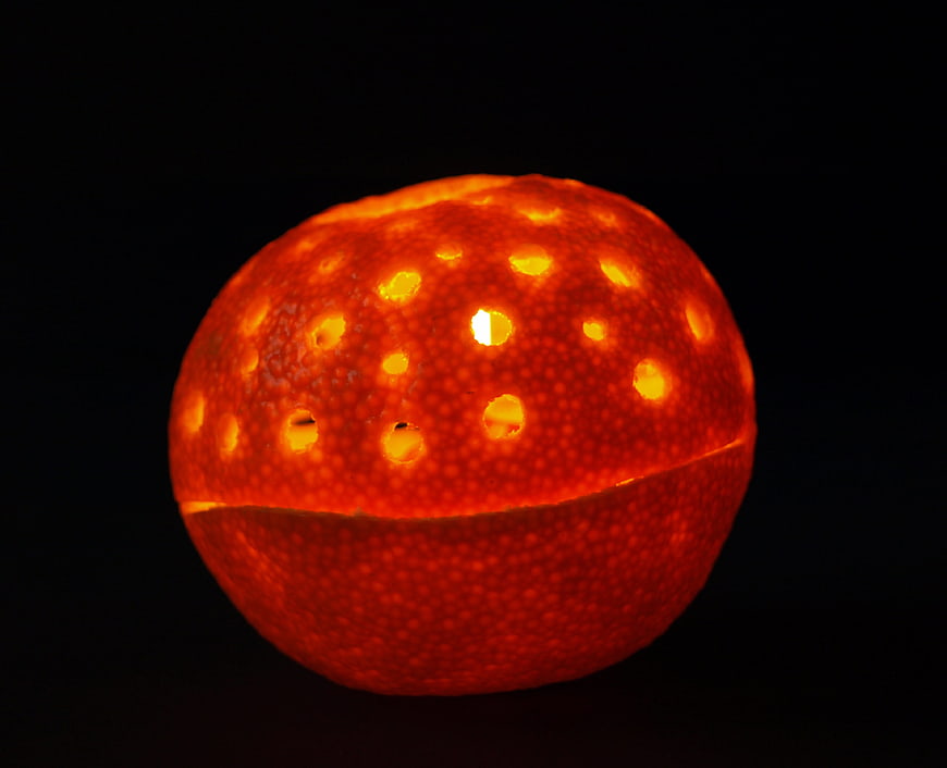 Glowing orange fruit lantern with holes on black background