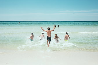Group of friends jumping into ocean waves on sunny beach
