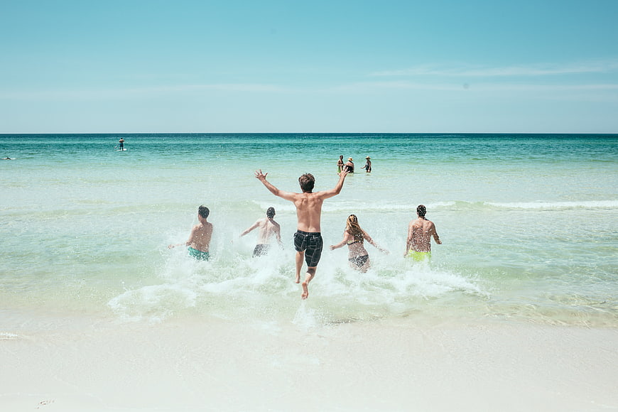 Group of friends jumping into ocean waves on sunny beach