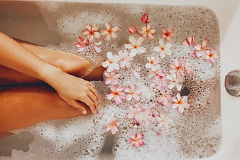 Woman relaxing in bubble bath with pink frangipani flowers