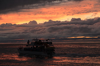 Silhouette of tour boat on ocean during dramatic sunset