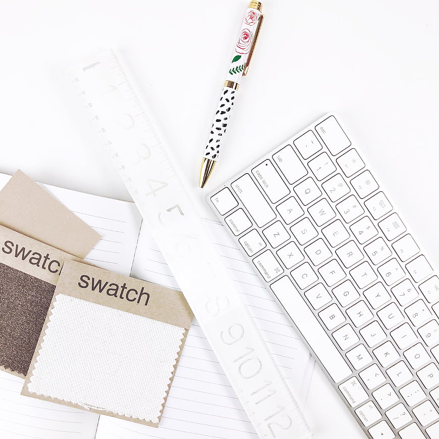 Minimalist white desk setup with keyboard, pen, and fabric swatches