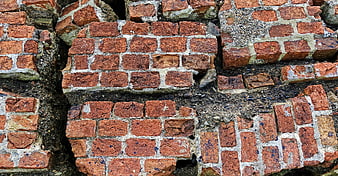 Close-up of weathered red brick wall with cracks and decay