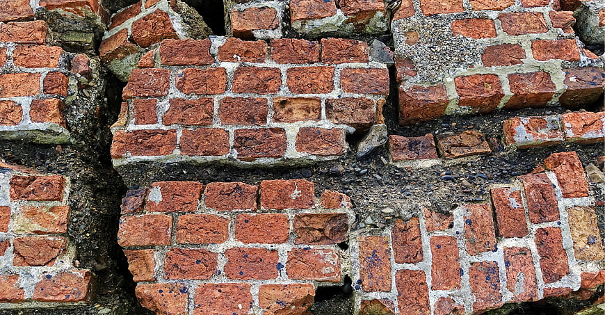 Close-up of weathered red brick wall with cracks and decay