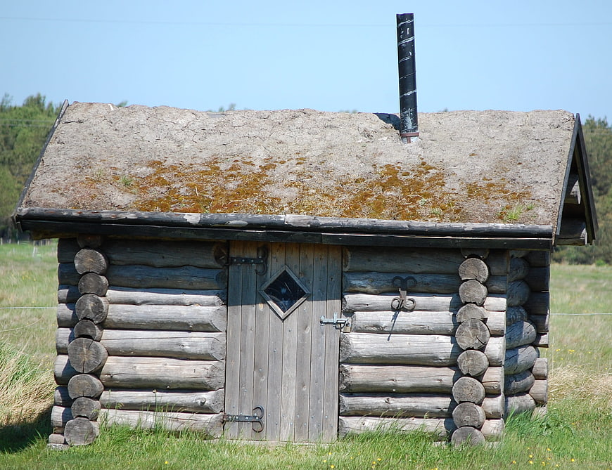 Old rustic log cabin with thatched roof in summer field