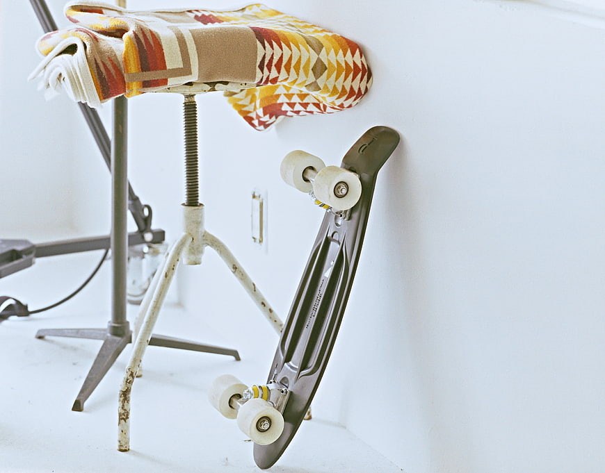 Vintage skateboard leaning against white wall near stool