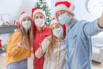 Friends taking a selfie with face masks and Santa hats at Christmas