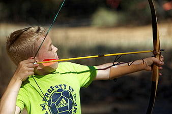 Young boy aiming a traditional wooden bow and arrow outdoors