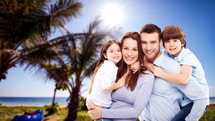Happy family of four hugging on sunny tropical beach