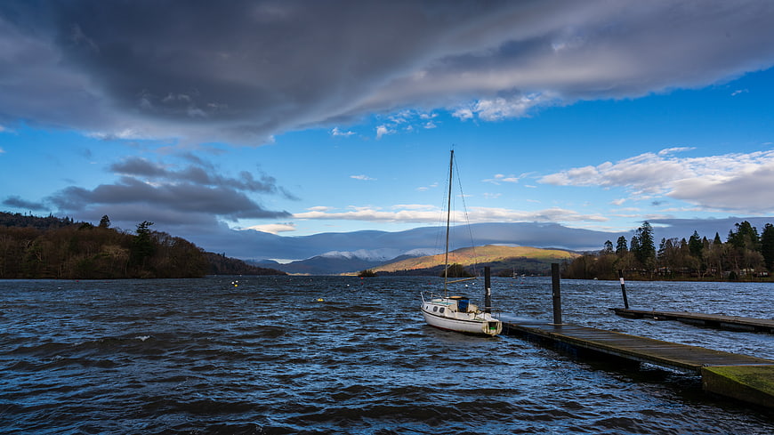 Sailboat Docked at Wooden Pier on Lake with Mountains