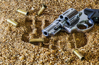 Chrome revolver and bullets on sand with skull outline