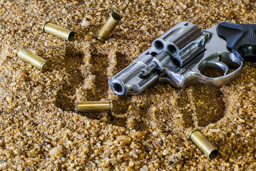 Chrome revolver and bullets on sand with skull outline