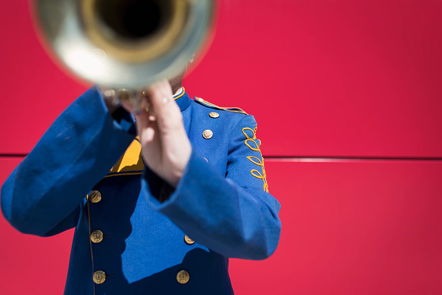 Marching Band Member Playing Trumpet Against Red Wall