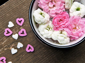 Pink and white flowers in a bowl with heart decorations on wood