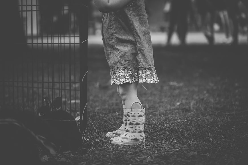 Child in Rain Boots Standing Near Rabbit Cage