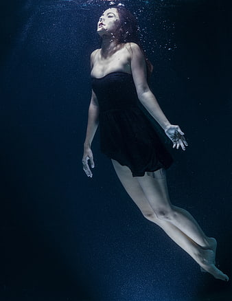 Woman in black dress floating underwater with bubbles
