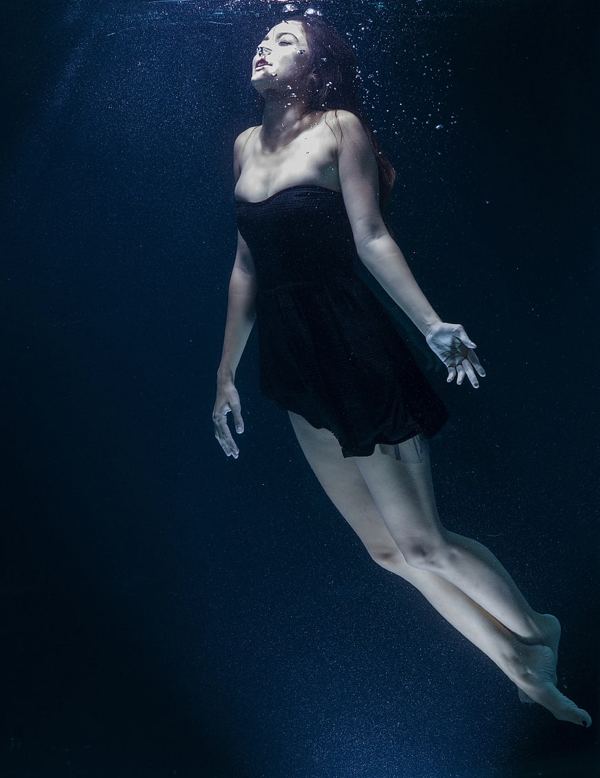 Woman in black dress floating underwater with bubbles