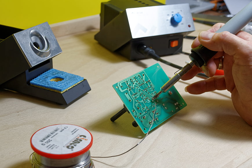 Close-up of electronics technician soldering a green circuit board