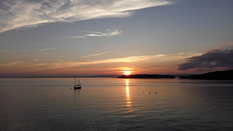 Serene sunset over calm water with sailboat silhouette