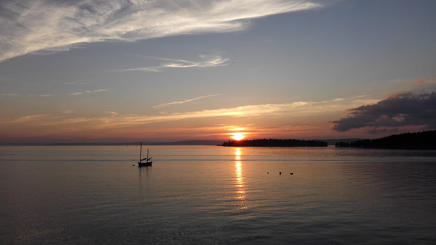Serene sunset over calm water with sailboat silhouette