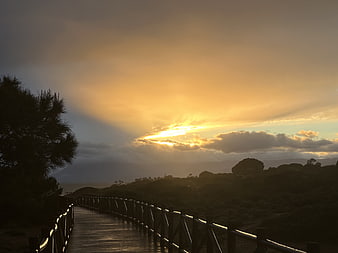 Sunset over wooden boardwalk with dramatic clouds and silhouette