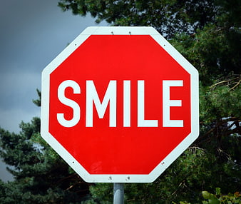 Red Stop Sign with Smile Text Against Trees
