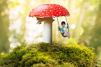Cute child swinging on giant red mushroom in fantasy forest