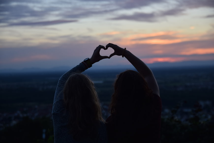 Two women making heart shape with hands at sunset