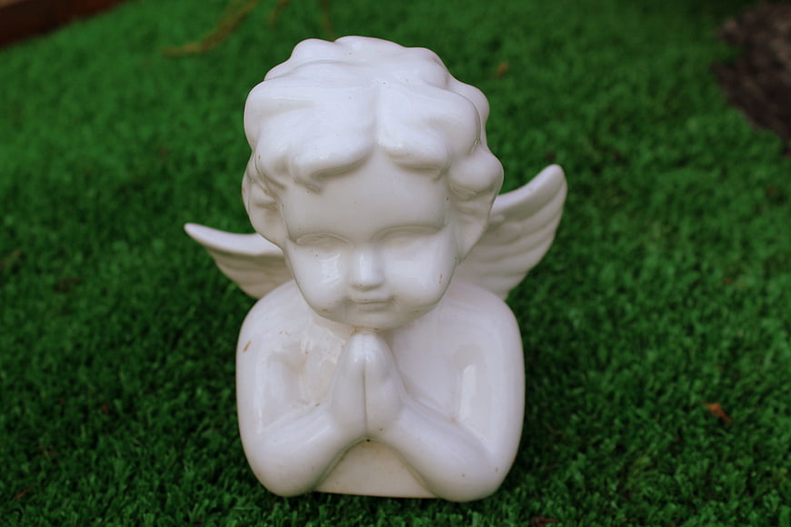 White porcelain praying angel figurine on green moss