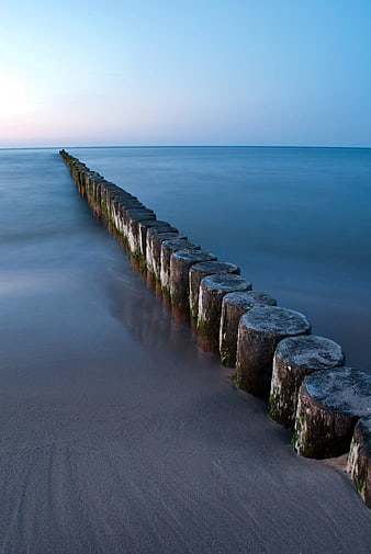 Long Exposure Wooden Breakwater Poles on Calm Blue Beach