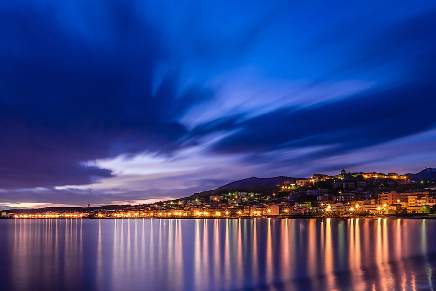 Coastal Town Night Skyline with Dramatic Clouds and Water Reflections