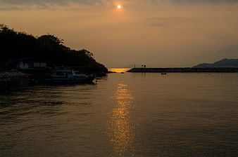 Golden sunset over calm harbor with boat silhouette