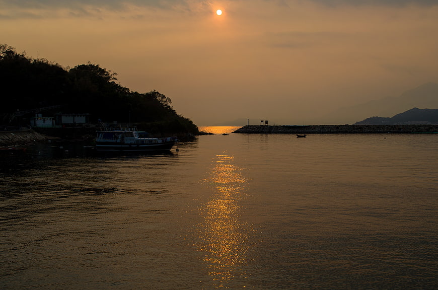 Golden sunset over calm harbor with boat silhouette