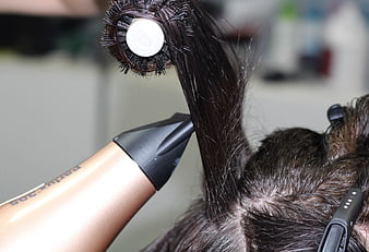 Close-up of hairstylist blow-drying and brushing dark hair in salon