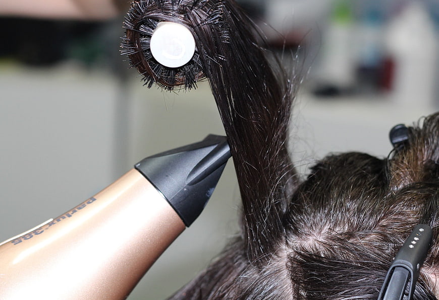 Close-up of hairstylist blow-drying and brushing dark hair in salon