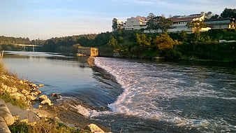 River weir with flowing water and hillside houses
